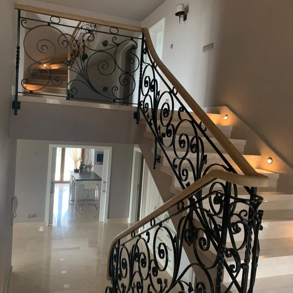 Elegant wrought iron staircase balustrade with intricate scroll patterns and a smooth timber handrail in a modern luxury home.