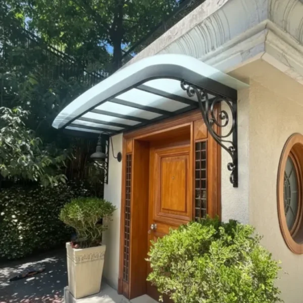Classical arched door canopy with black wrought iron scroll brackets and a frosted glass roof, installed over a wooden entrance door in a garden setting.