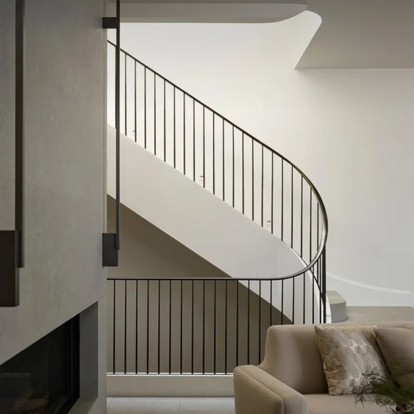 Bespoke minimalist black wrought iron staircase railing with thin vertical bars and a seamless curved handrail in a contemporary interior.